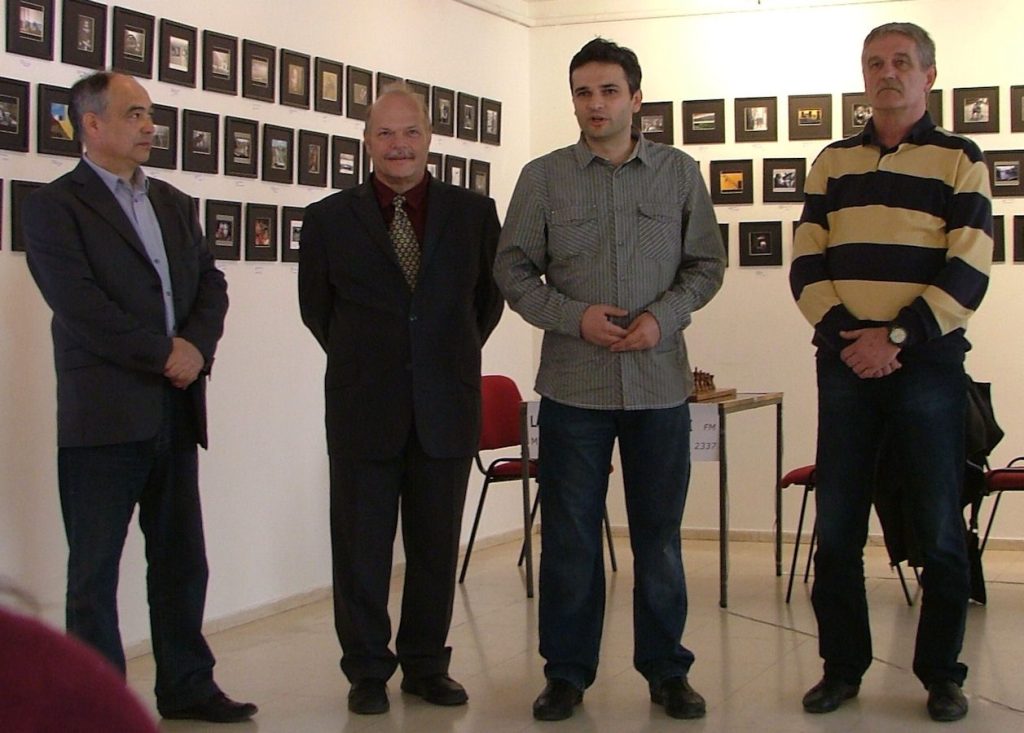 Četiri čoveka stoje u prostoriji sa uramljenim slikama na zidu