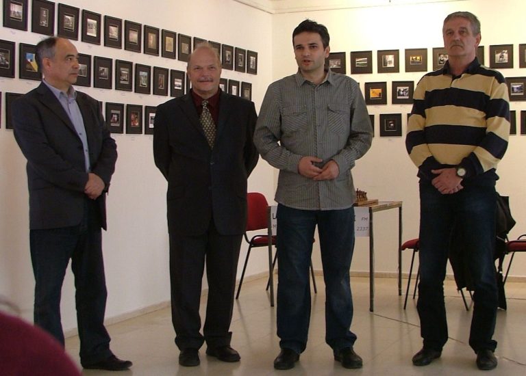 Četiri čoveka stoje u prostoriji sa uramljenim slikama na zidu